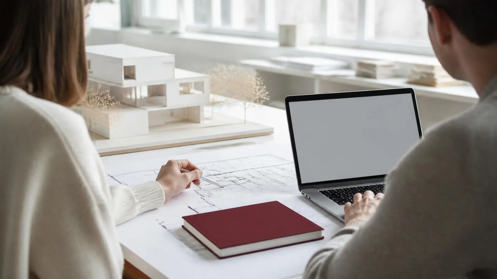Deux personnes de dos devant un plan imprimé et un ordinateur portable, dans une agence d'architecture.
